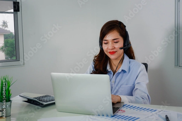 Fototapeta Happy asien young business woman wearing wireless headphones, looking at computer screen, waving hello. Pleasant attractive mixed race female professional holding video call with client.