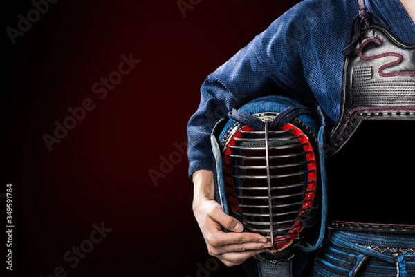 Fototapeta male in in tradition kendo armor with helmet in hand. shot in studio. isolated on dark red background