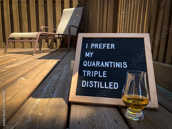 Obraz Wooden restaurant or pub sign with "quarantini" and "triple distilled" placed on a wood deck. Lounge chair in the background. Felt letter board with white letters. Covid-19 pandemic joke or meme.