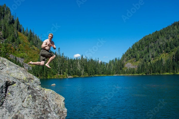 Fototapeta Adventurous male hiker jumping into an alpine lake in Washington State.
