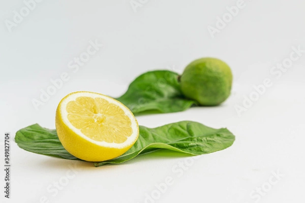 Fototapeta Half Organic Lemon and a lime with lemon tree leaves isolated on white. Fresh summer background.