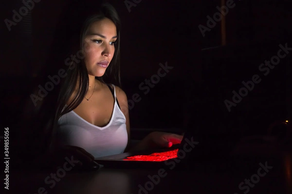 Obraz Beautiful latina gaming girl plays game on gaming notebook PC in dark area