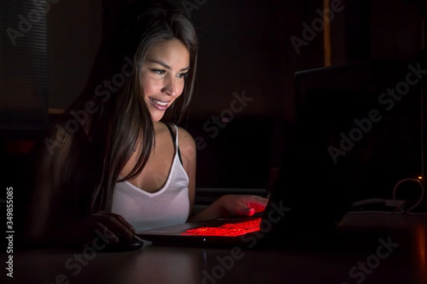 Obraz Beautiful latina gaming girl plays game on gaming notebook PC in dark area
