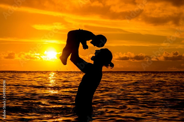 Fototapeta Father throws up a little son against the backdrop of the ocean and an incredible sunset