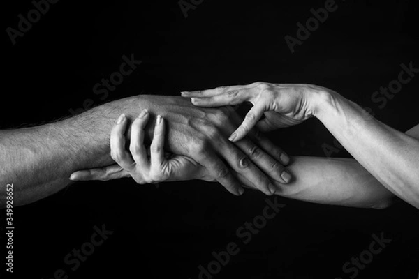 Obraz a woman gently holds a man's hand in her own against a dark background. close up. black and white photo