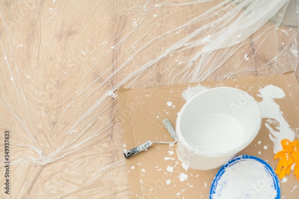 Obraz Almost empty paint bucket surrounded by paint blobs and paint residues on painter's film and cardboard Paint roller Latex gloves Handicraft training Apartment renovation Parquet floor