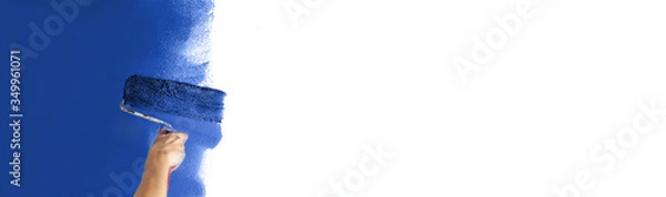 Obraz Human hand with a large roller of paint begins to paint a white wall. Handicraft training contrast color sample color test tool renovation blue maritime dark blue