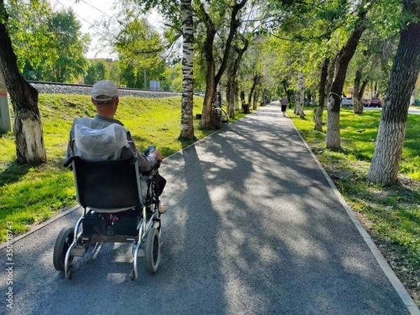 Obraz an unrecognizable disabled man in a wheelchair Park. a lone disabled person in an electric wheelchair moves along an empty summer alley.