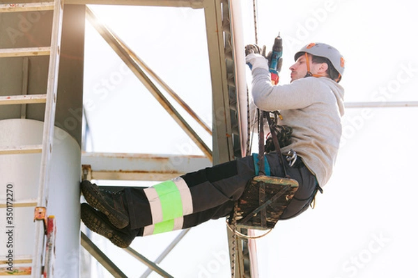 Fototapeta Industrial climber in helmet and overall working on height. Risky job. Professional worker