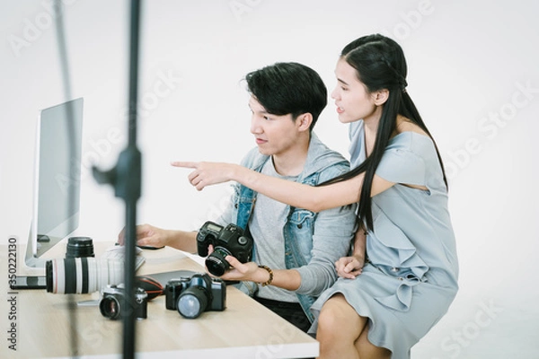 Fototapeta An Asian photographer and an Asian model are looking at pictures taken on a computer monitor, in a photo studio after the work is done.Review and check the quality of the photos,