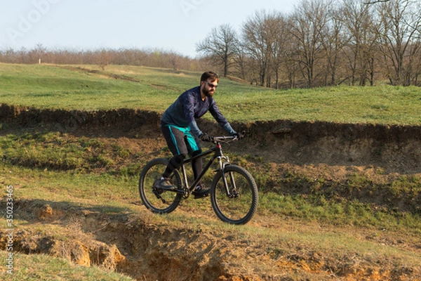 Fototapeta Cyclist in shorts and jersey on a modern carbon hardtail bike with an air suspension fork standing on a cliff against the background of fresh green spring forest