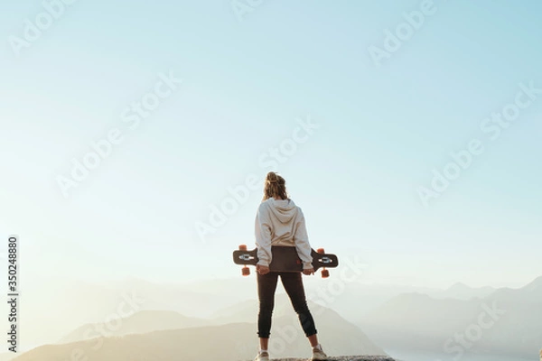 Fototapeta .Young long boarder woman with dreadlocks  standing on top of mountain in beautiful scenic nature in Montenegro at sunset. Freedom concept.