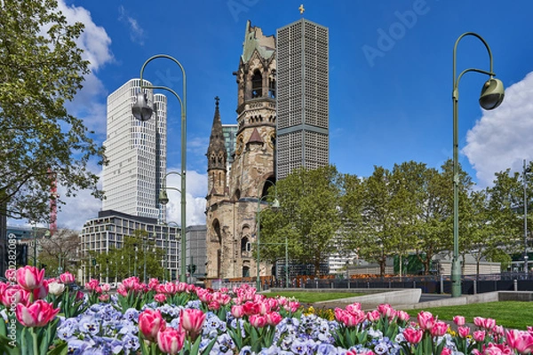 Fototapeta berlin niemcy, Kościół Pamięci Cesarza Wilhelma, po niemiecku Kaiser-Wilhelm-Gedächtniskirche, wiosna w mieście, z błękitnym niebem i kolorowymi kwiatami, zielone drzewa na poboczu drogi
