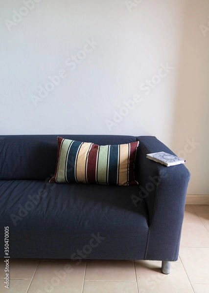 Obraz Sofa in dark blue with a colorful striped throw pillow and a book on the arm.  In a white paint wall room.