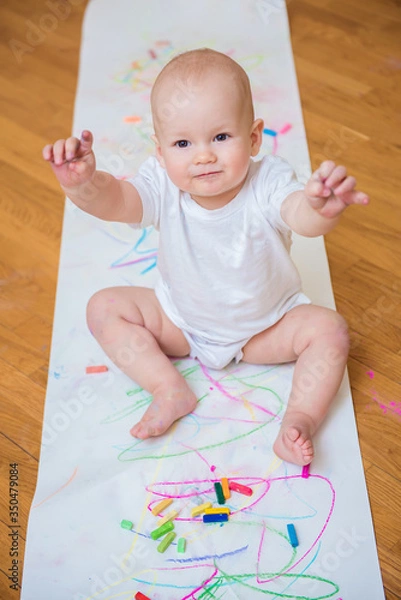 Fototapeta Little cute child with creativity draws with crayons at home on a sheet of white paper. The concept of children's early development of creativity
