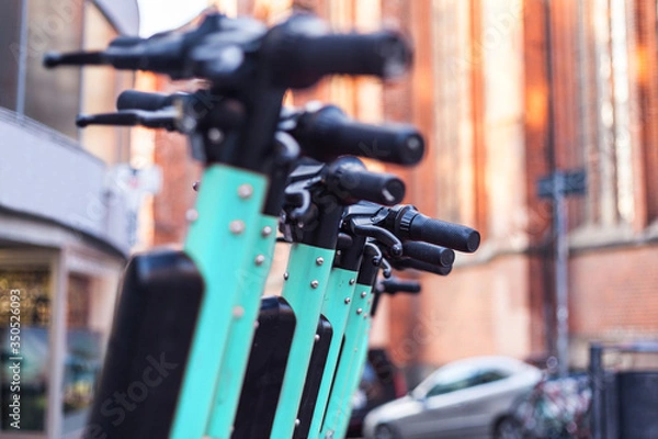 Obraz E-scooters or electric scooters are lined up in a row on the street corner in a big city e-mobility e-scooter mobile office means of transport environmentally friendly alternative new cityscape