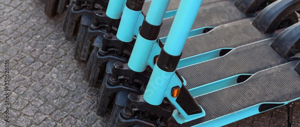 Obraz E-scooters or electric scooters are lined up in a row on the street corner in a big city e-mobility e-scooter mobile office means of transport environmentally friendly alternative new cityscape