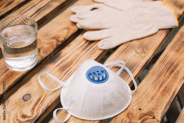 Obraz Mask, gloves are lying on the wooden table background. Glass of water is standing on the wooden background. Safety.