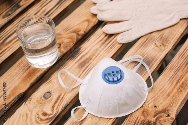 Obraz Mask, gloves are lying on the wooden table background. Glass of water is standing on the wooden background. Safety.