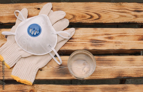 Obraz Mask, gloves are lying on the wooden table background. Glass of water is standing on the wooden background. Safety.