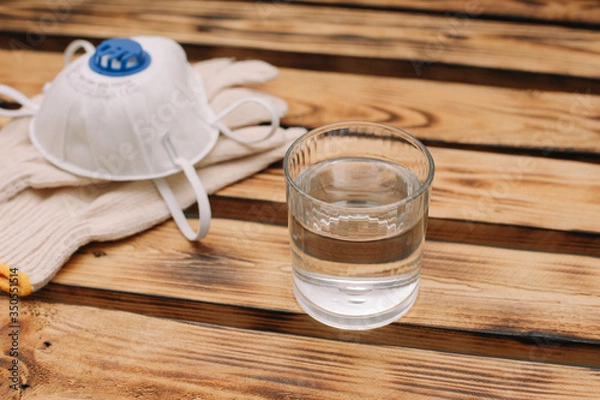 Obraz Mask, gloves are lying on the wooden table background. Glass of water is standing on the wooden background. Safety.