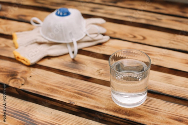 Obraz Mask, gloves are lying on the wooden table background. Glass of water is standing on the wooden background. Safety.