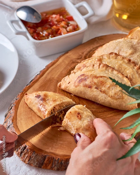 Fototapeta Cutting with a knife Empanadas argentinas traditional food with sauce on wooden ray