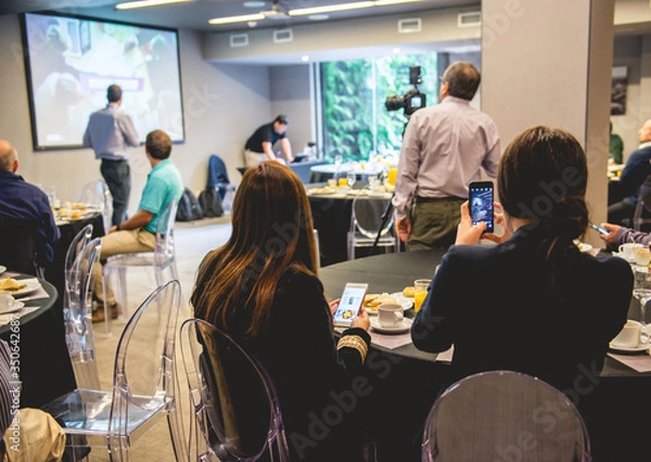 Obraz Businessmen, businesswoman and workers from back seated, recording and listen a seminar with breakfast in a hotel salon