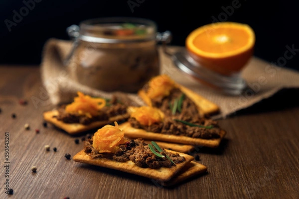 Obraz A few crackers with poultry liver pate and orange jam, sliced orange fruits on the sackcloth and wooden background