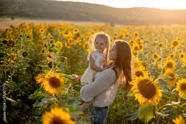 Obraz Piękna matka i córka spacerują latem i przytulają się na słonecznikowym polu