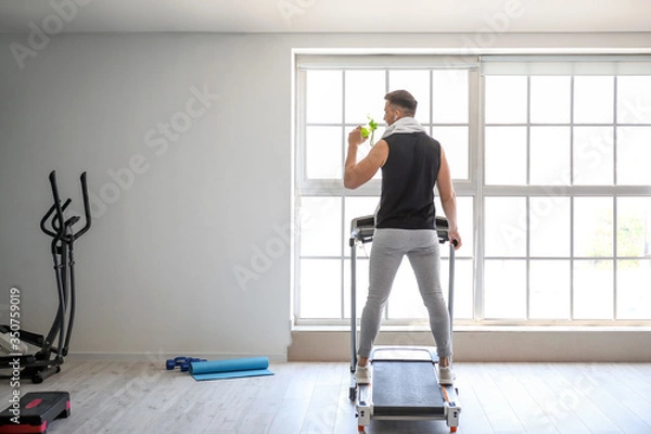 Fototapeta Young man drinking water after training in gym