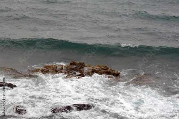 Fototapeta small waves at the stormy sea, with stones