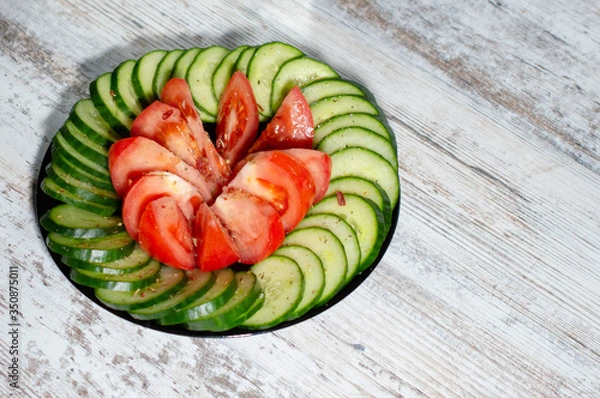 Fototapeta chopped cucumbers and tomatoes in a black plate on a light wood background