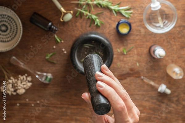 Fototapeta Close up of woman using pestle and mortar.  Table out of focus with range of ingredients relating to beauty and skin care.  Top down view of beauty background.