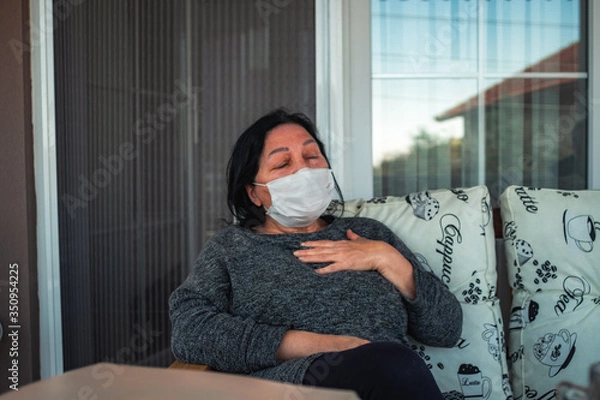 Fototapeta Middle aged caucasian woman with medical face mask, resting on cpuch on veranda during COVID-19 threat. Woman with mask on her terrace is resting, sleeping, looking, talking.