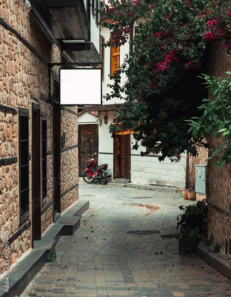 Fototapeta Narrow street in Antalya’s old town with rectangular billboard White mockup on the wall. Old town in city centrum is a must see place for tourists during their visit to Antalya.