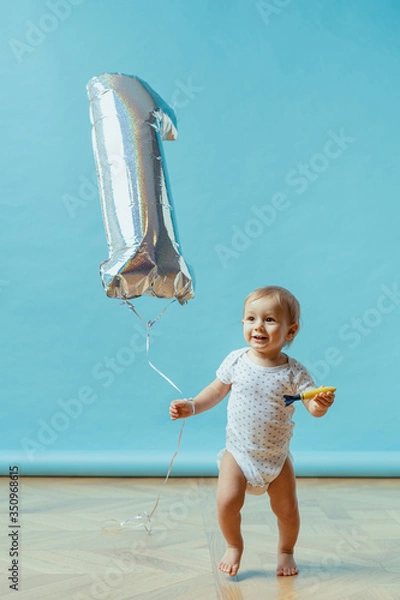 Fototapeta Funny kid running happy wearing pampers with one year balloon on blue background. First birthday celebration copy space