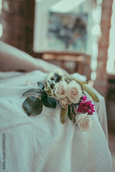 Fototapeta A close-up composition of white roses and purple hyacinth on a linen sheet. Floral and wellness concept. Tender morning decor. Flowers on a white tablecloth and silhouette of female legs.. Soft focus