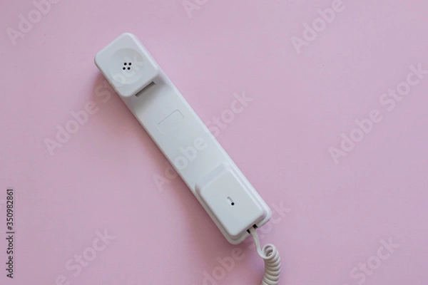 Fototapeta A close up view of A white vintage dial telephone handset on pink background. A retro receiver with phone curly wire and copy space. Office context. Call center. Communication device.