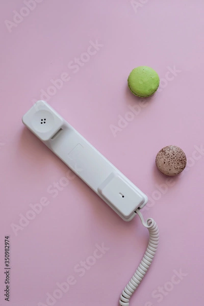 Obraz A close up view of A white vintage dial telephone handset and two macaronis on pink background. Communication device. A retro receiver with phone curly wire and copy space. Office context. Call center