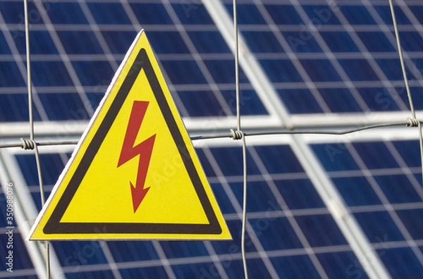 Obraz Solar power farm station on a background selective focus on a yellow triangular high voltage warning sign. The inscription in Russian "Do not come near kill"