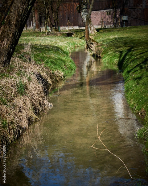 Fototapeta A quiet stream meanders around meadows and fields