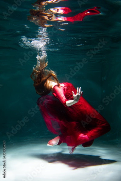 Fototapeta Beautiful girl underwater in a red dress swims in the pool. Tenderness and elegance. Bubbles and a lot of water