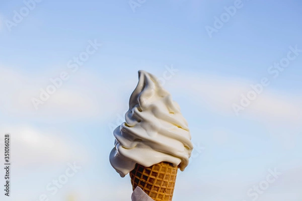 Fototapeta vanilla ice cream cone melting on a sunny say with the sky background  holding it it to the sky summer day stock photo 