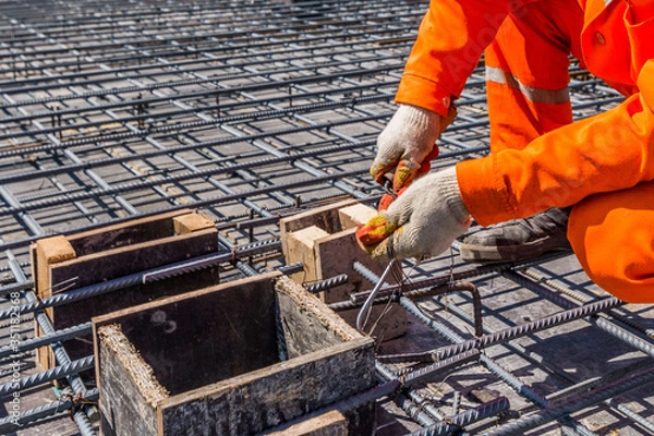 Obraz a construction worker in gloves and uniform twists the mesh under the pouring of concrete