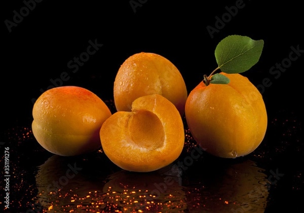 Fototapeta Apricots with green leaves on a black background.