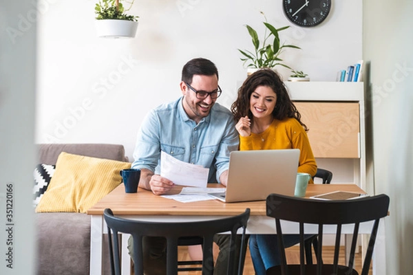 Fototapeta Happy husband and wife read good news online at laptop, smiling man holding documents receiving positive decision from bank