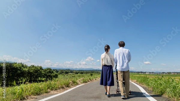 Obraz 自然の中ベビーカーを押し散歩する若い夫婦の後ろ姿