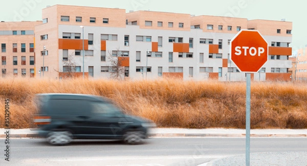 Fototapeta Panning of black van with city in the background, with dry field and clear sky and STOP sign