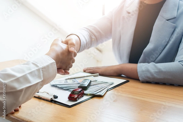 Fototapeta Car sales agent and client shaking hand after finishing signed the car rental agreement in the office.